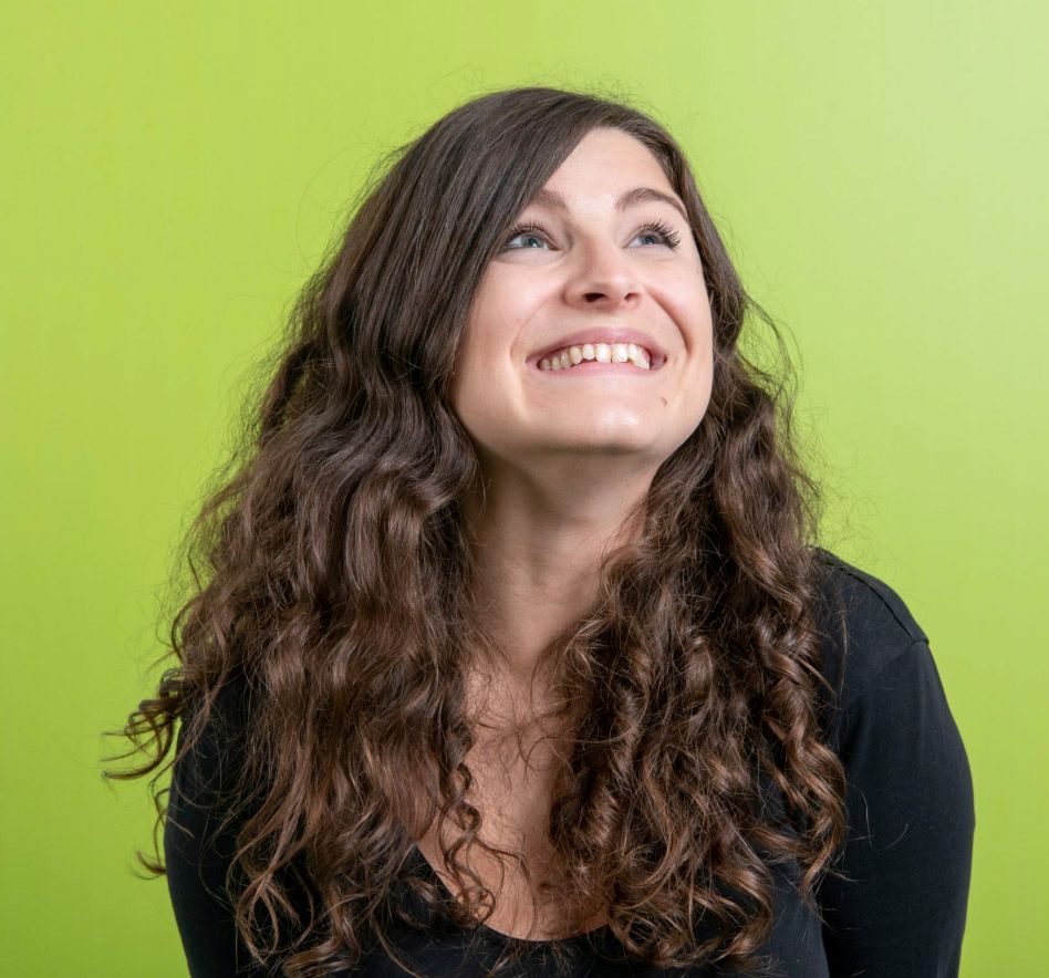 Young woman with long curly brown hair smiling and looking up against a bright green background.
