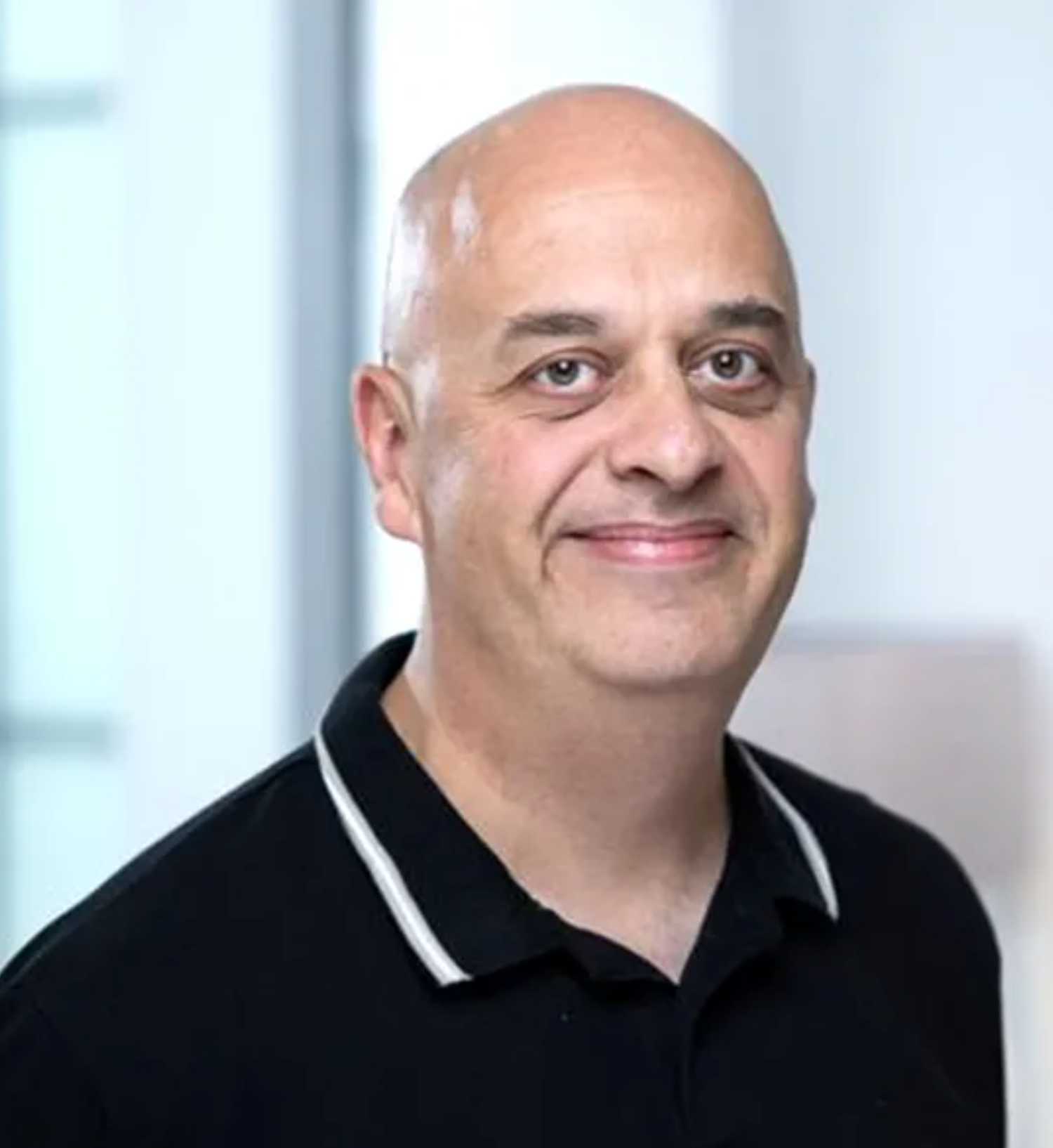 Professional headshot of a bald middle-aged man smiling, wearing a black polo shirt with white trim.