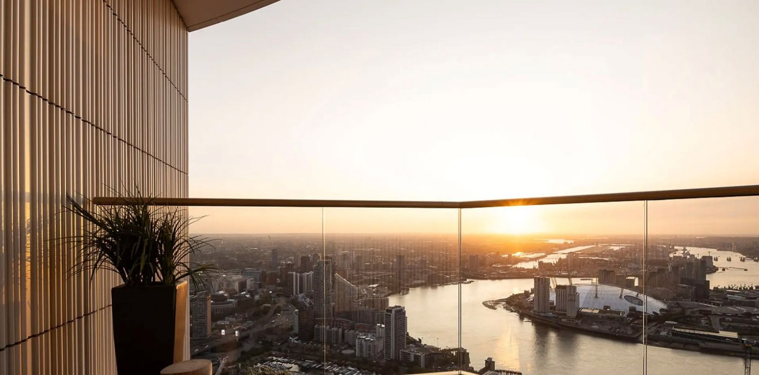 Luxury high-rise balcony with glass railing overlooking a stunning river cityscape at golden sunset.