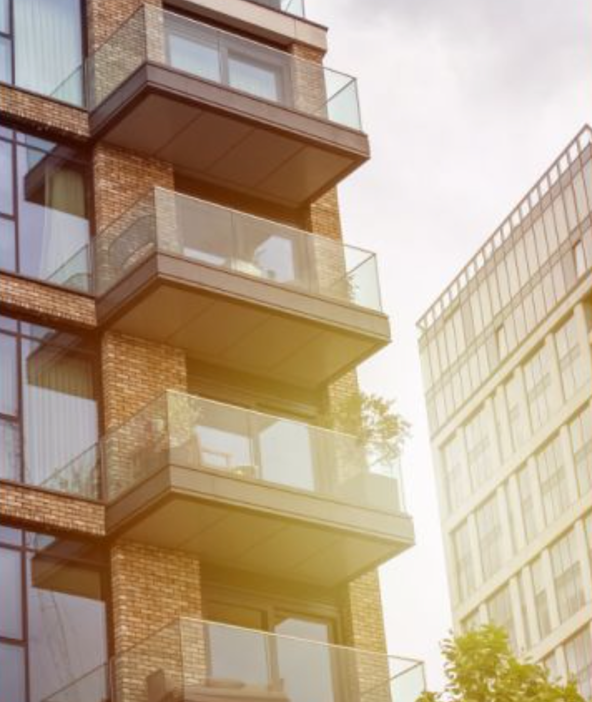 Modern brick apartment building with glass balconies reflecting sunlight against a cloudy urban sky.
