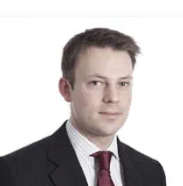 Professional headshot of a young businessman in a dark suit and burgundy tie against a white background.