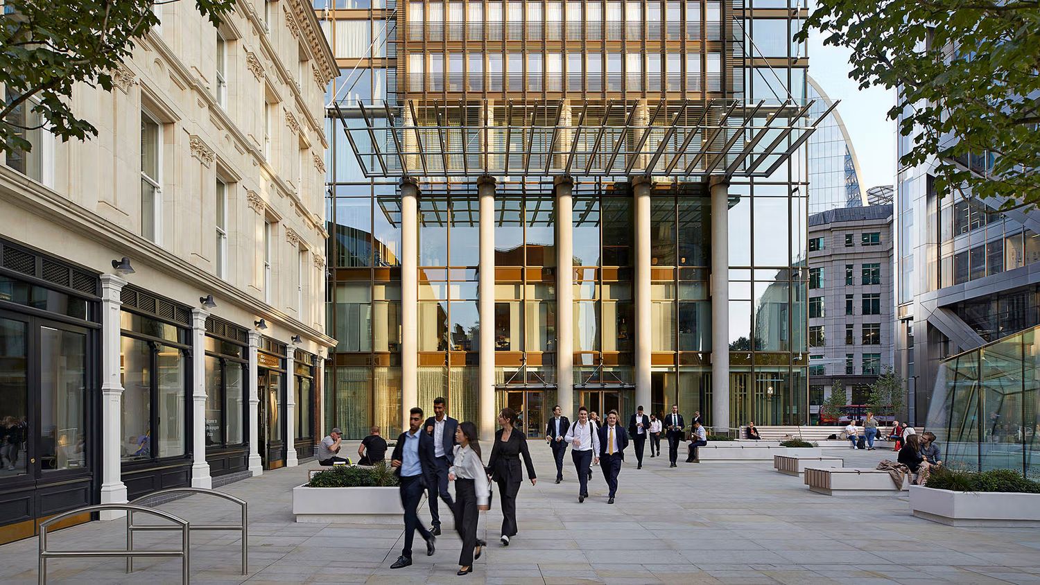 Modern glass office building entrance with business professionals walking through an open plaza in London.
