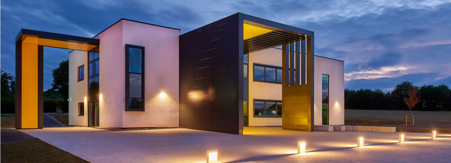 Modern two-story luxury home exterior illuminated at dusk with warm yellow accent lighting and contemporary architectural design.