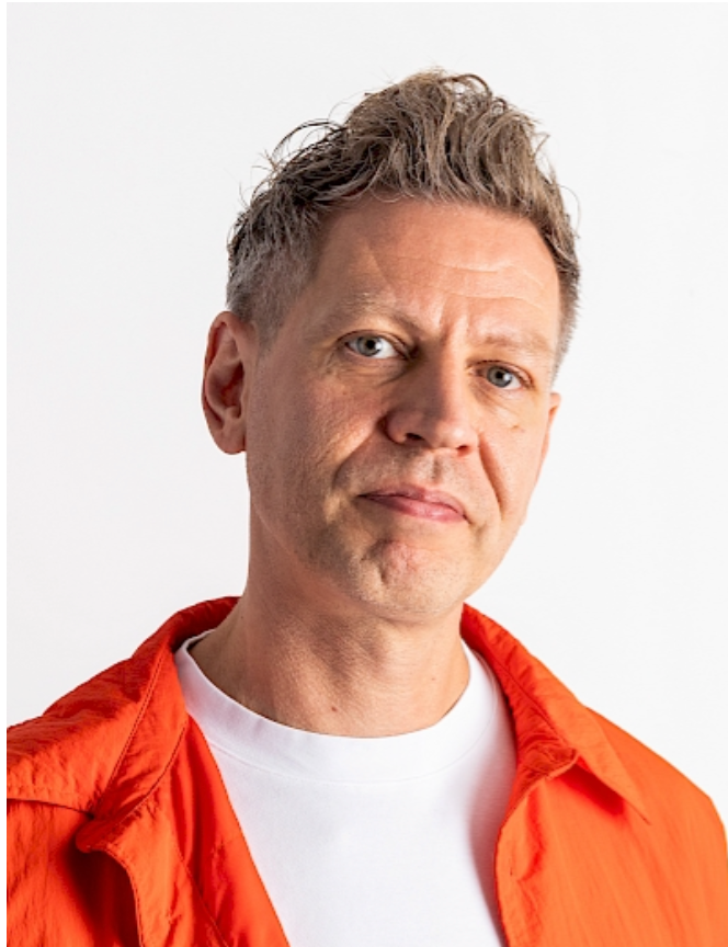 Middle-aged man with short gray hair wearing an orange jacket over a white t-shirt against a white background.