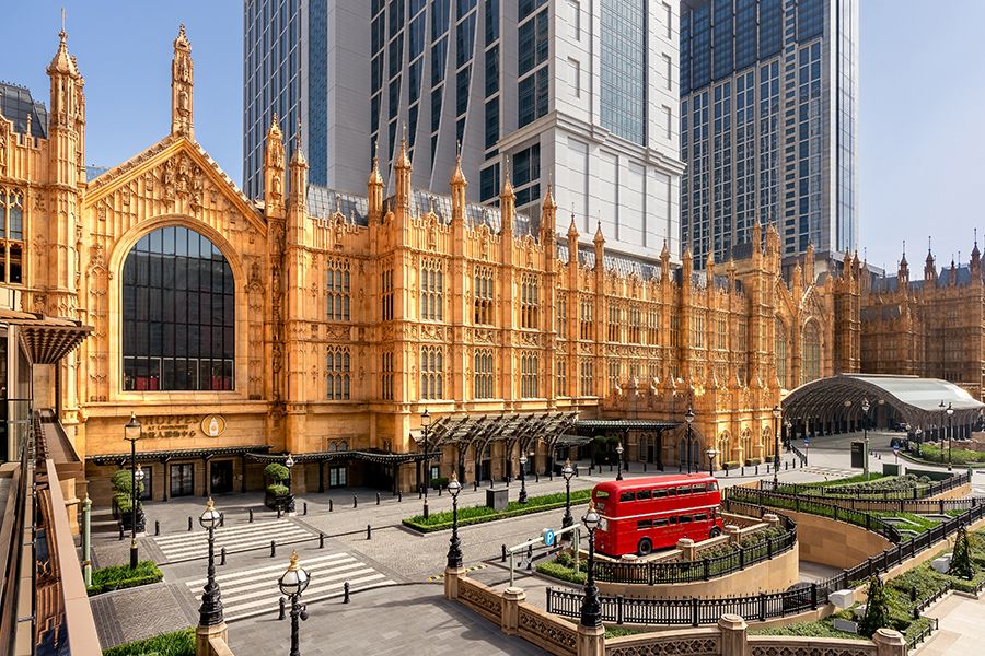 Gothic-style luxury hotel facade with ornate golden stonework, featuring a red double-decker bus at the entrance in London.