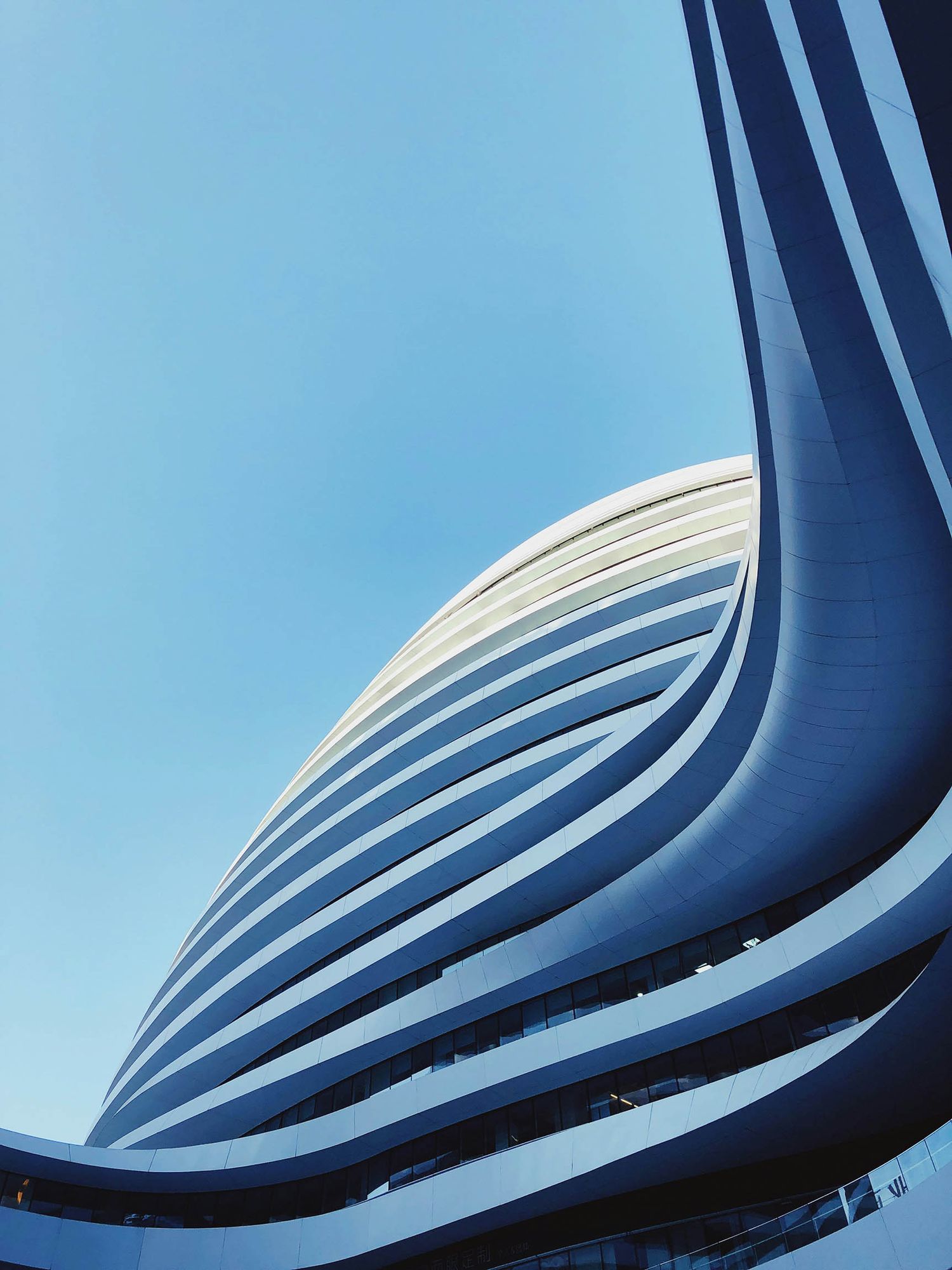 Low-angle view of a modern curved blue skyscraper with wave-like facade against a clear blue sky.