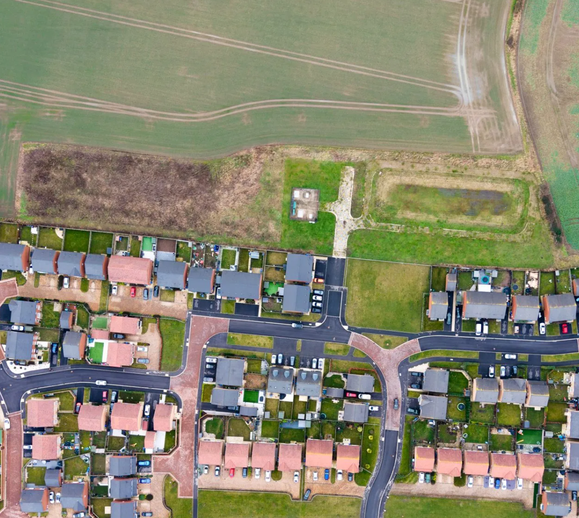 Aerial view of a residential neighborhood with houses, roads, and green fields in the UK.