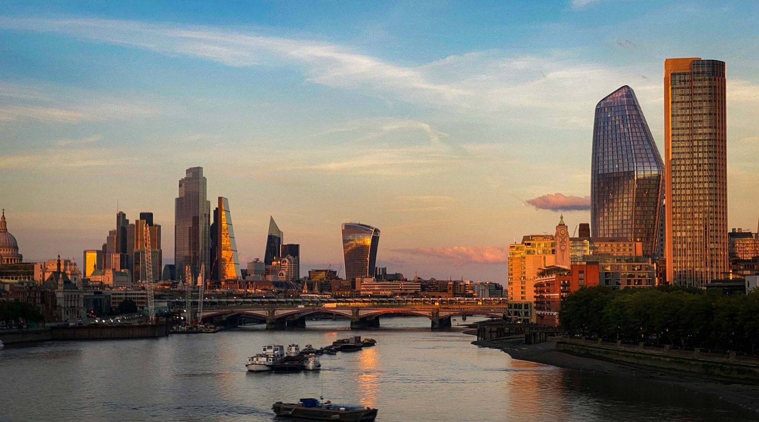 Golden hour skyline of London with the River Thames, bridges, and modern skyscrapers glowing under a vibrant sunset sky.
