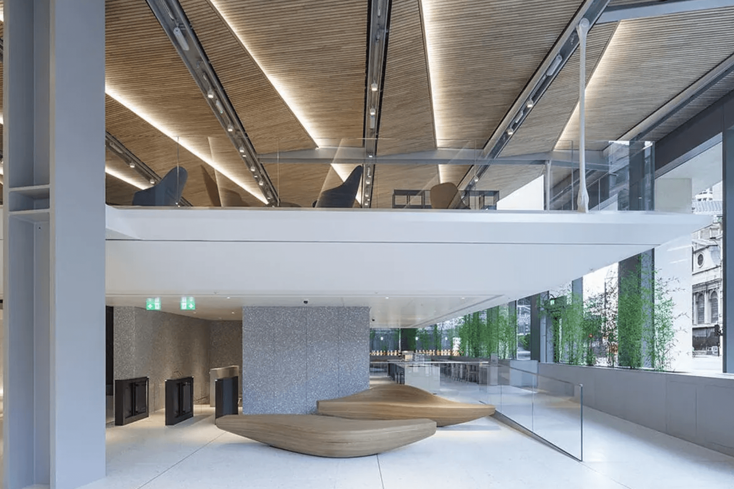 Modern building lobby with wooden ceiling, curved bench seating, glass railings, and lush green wall accents.