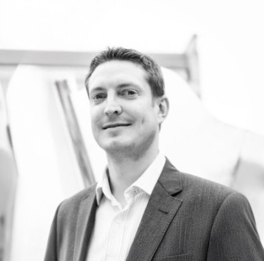 Professional businessman in a gray blazer smiling confidently in a modern office setting, black and white photo.