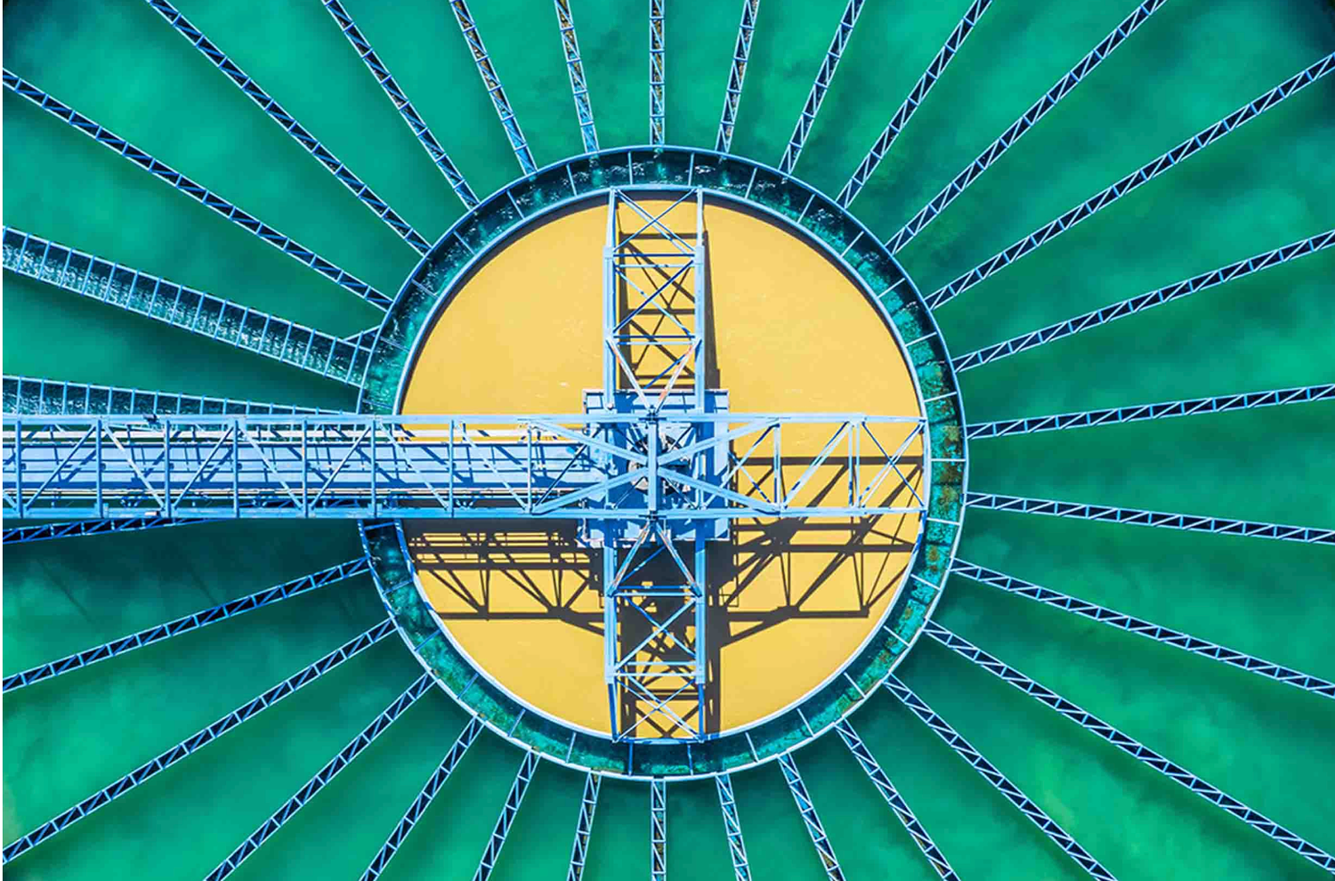 Aerial view of a circular green cooling tower with yellow center and blue steel cross structure.
