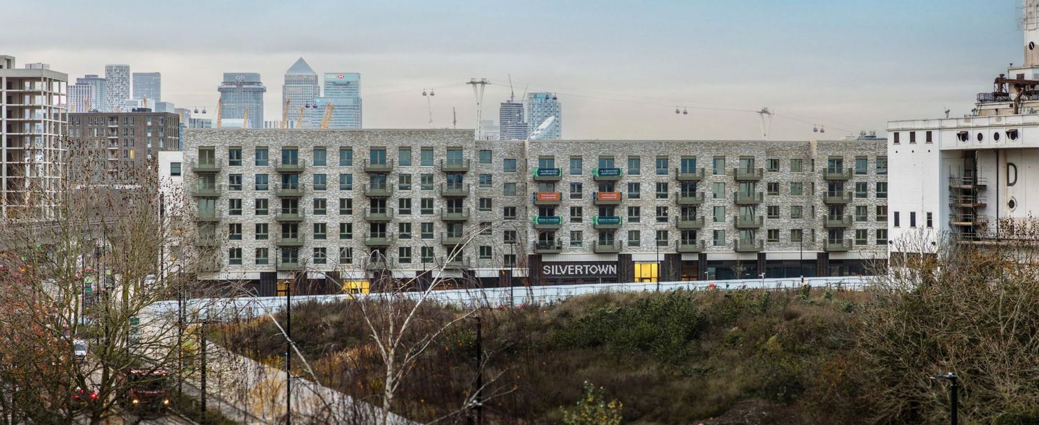 Modern apartment complex with city skyline backdrop, surrounded by bare trees in an urban landscape.