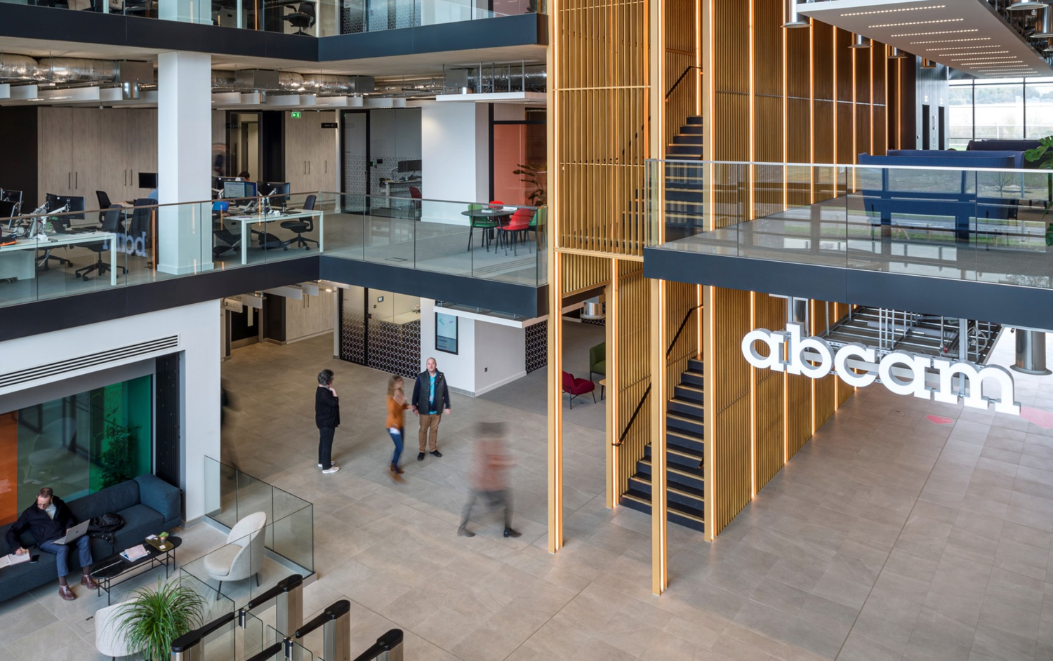 Modern office atrium with wooden columns, open floors, and the Adecco logo displayed prominently in a bright workspace.