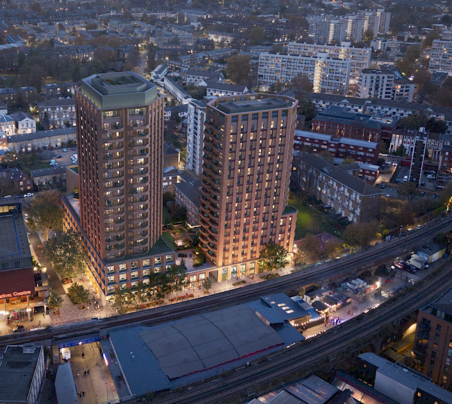 Aerial dusk view of two modern residential towers in brick, surrounded by urban cityscape and railway lines.