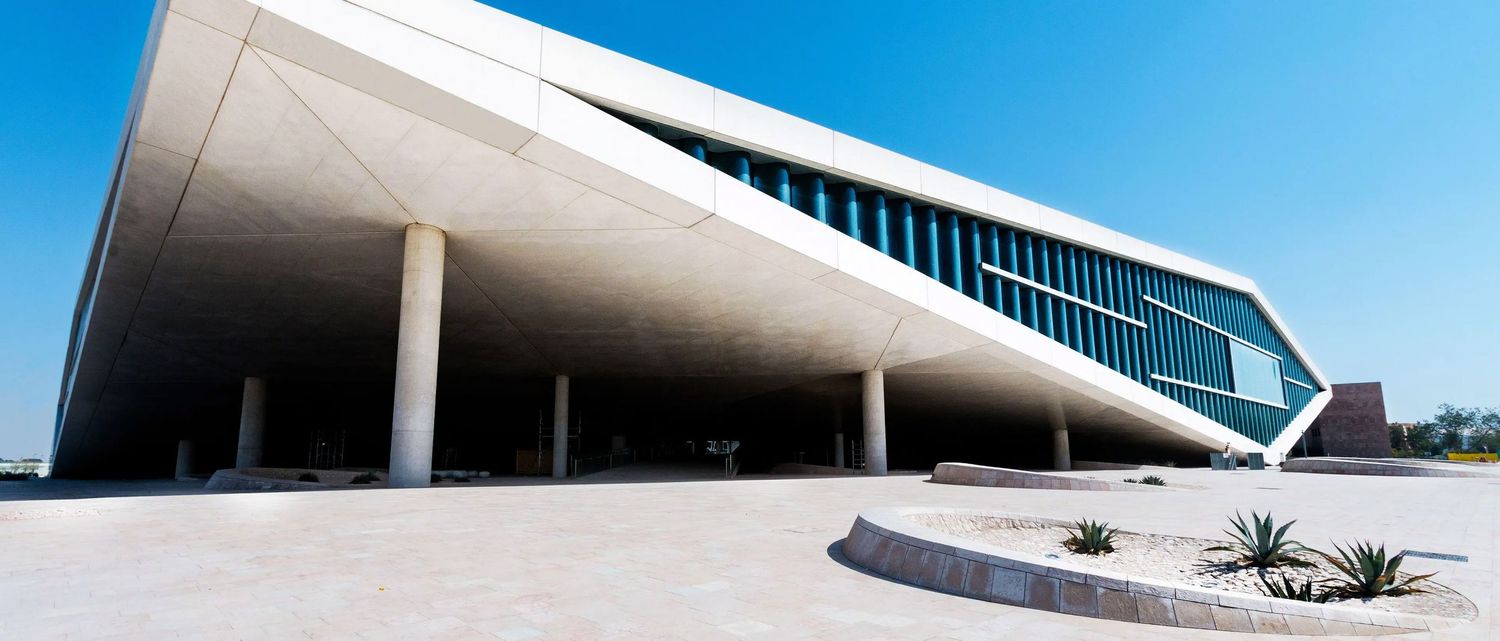 Modern angular white concrete building with large glass windows under a clear blue sky, showcasing contemporary architecture.