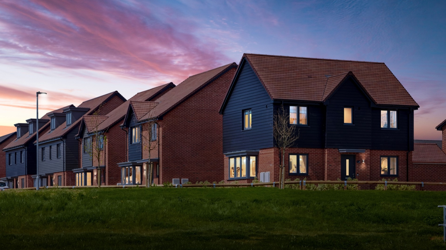 Modern residential homes with dark brick facades illuminated at dusk under a vibrant pink and blue sunset sky.