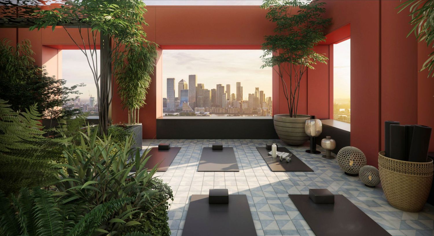 Rooftop yoga studio with red walls, lush greenery, meditation mats, and stunning city skyline views at sunset.