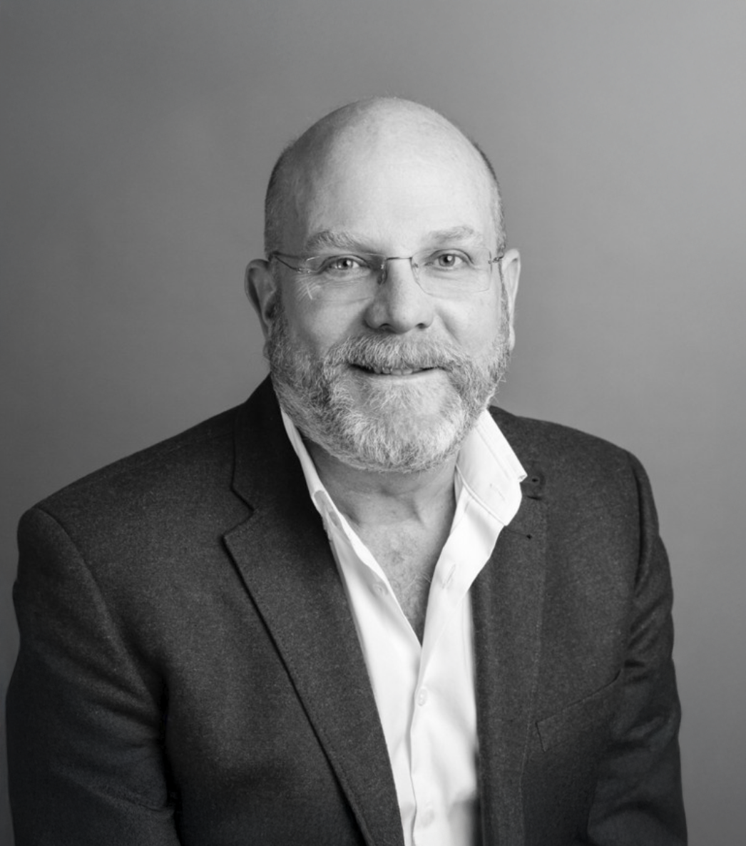 Black and white professional headshot of a bald man with glasses and a beard wearing a blazer.