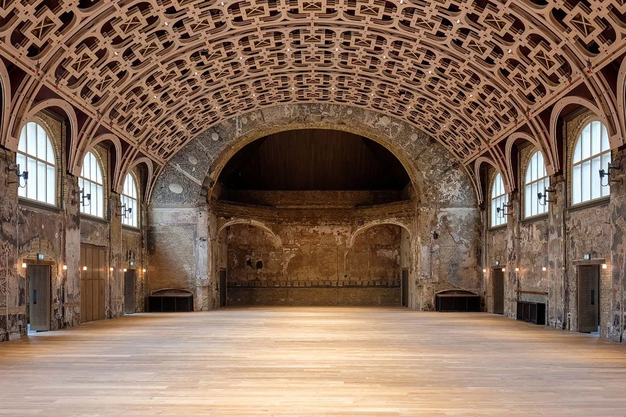 Grand historic hall with ornate vaulted ceiling, arched windows, and polished wooden floor in a medieval stone building.