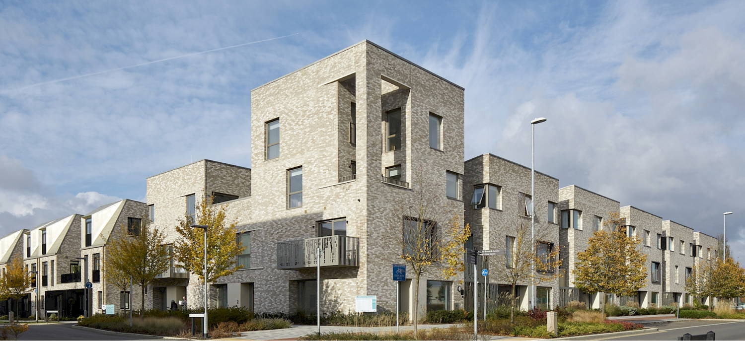 Modern brick residential complex with stepped facade design under cloudy sky, featuring balconies and landscaped surroundings.