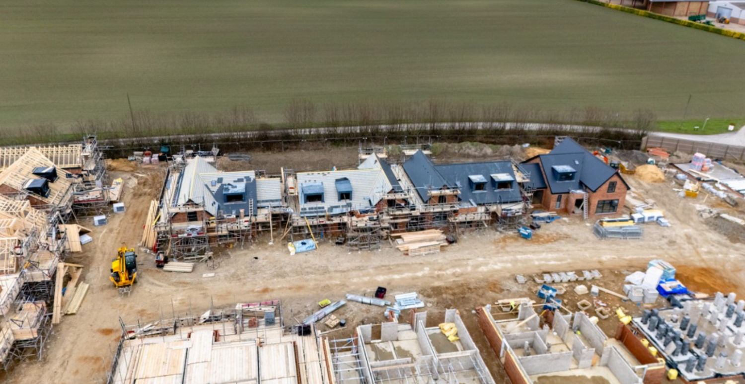 Aerial view of a residential construction site with multiple homes being built near a green field.