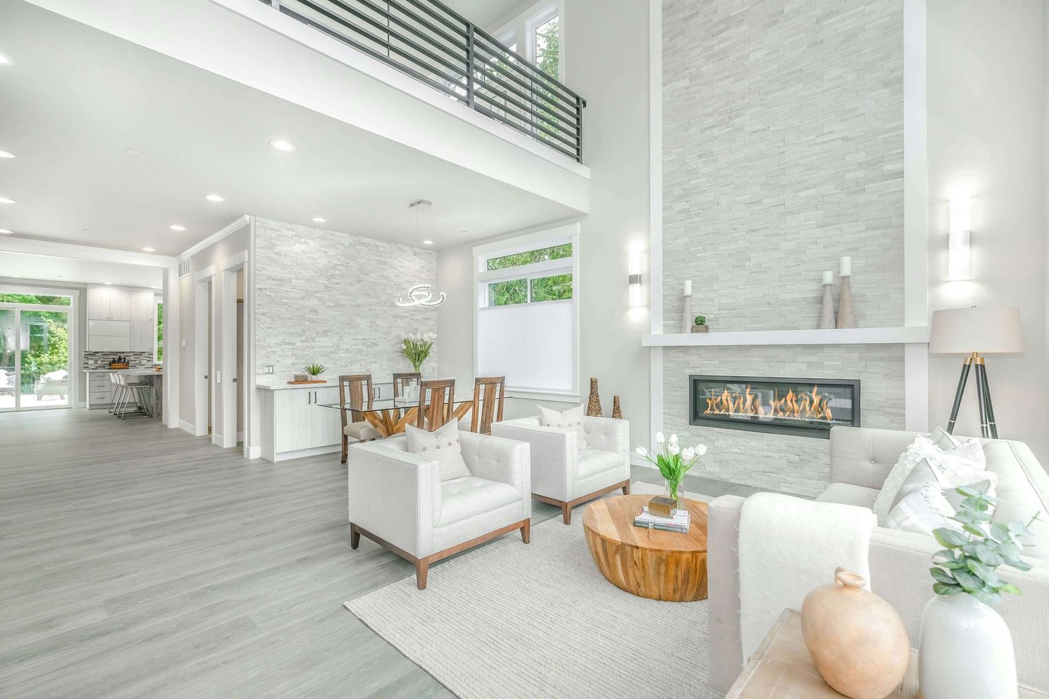Bright modern living room with white furniture, stone fireplace, high ceilings, and open floor plan with natural light.