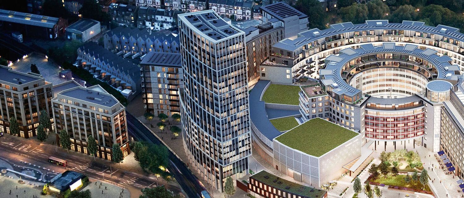 Aerial view of modern urban development featuring a tall glass tower and circular building with rooftop garden at dusk.