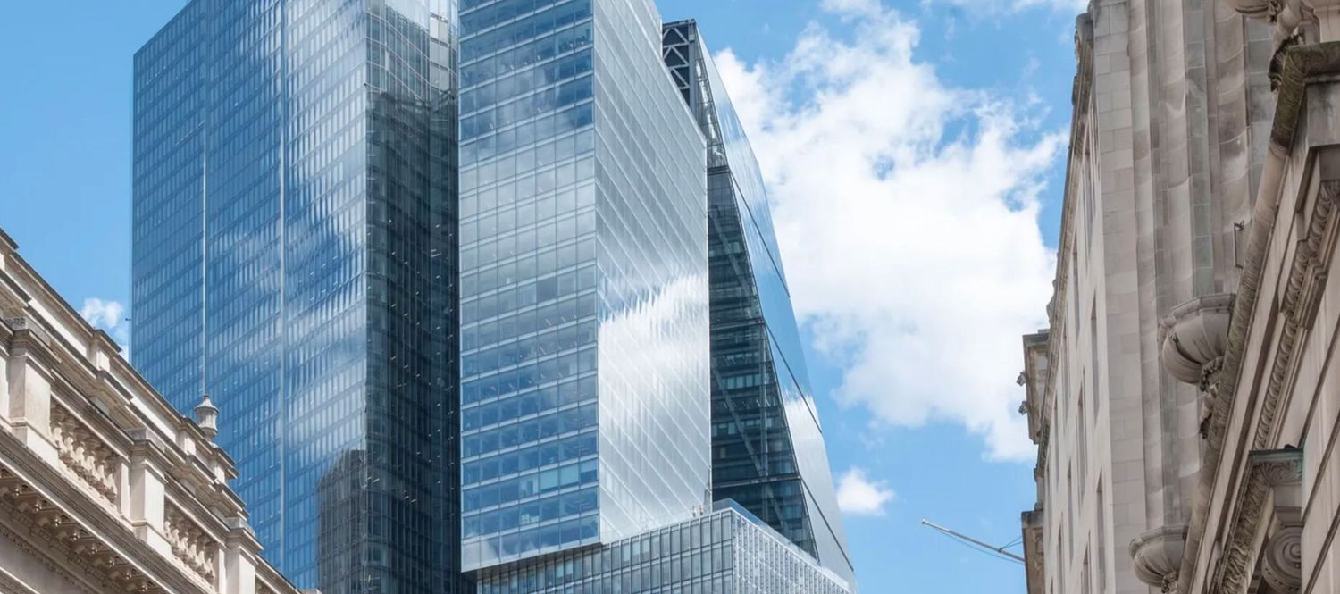 Modern glass skyscraper with reflective blue facade towering between classic stone buildings under a partly cloudy sky.