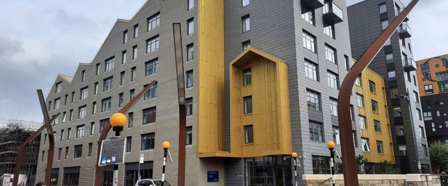 Modern mixed-use apartment building with yellow and grey facade panels in an urban development area.