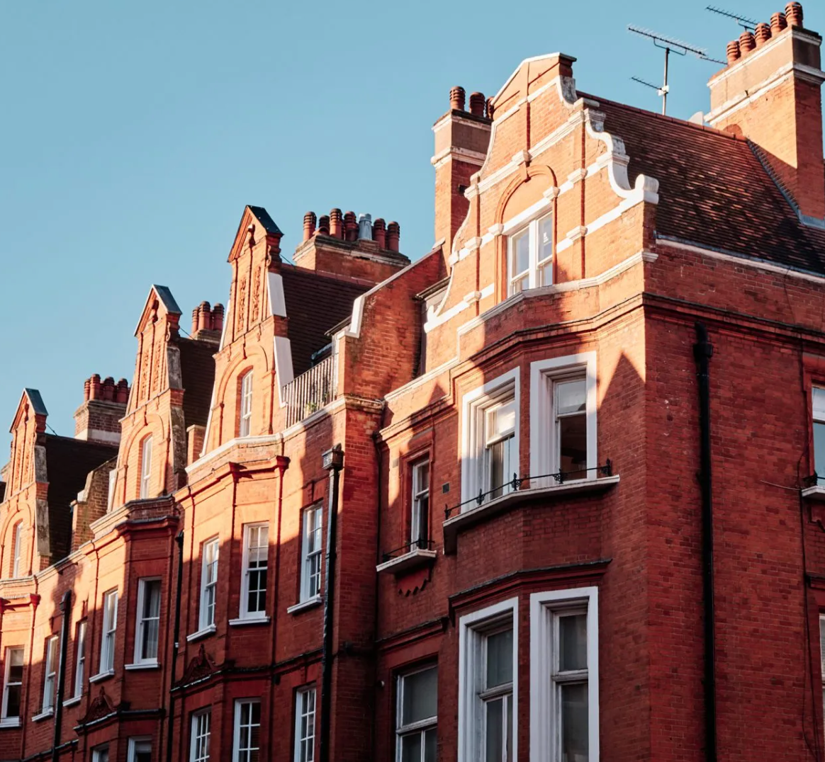 Row of Victorian red brick mansion flats with ornate gabled rooflines and white trim under blue sky in London.