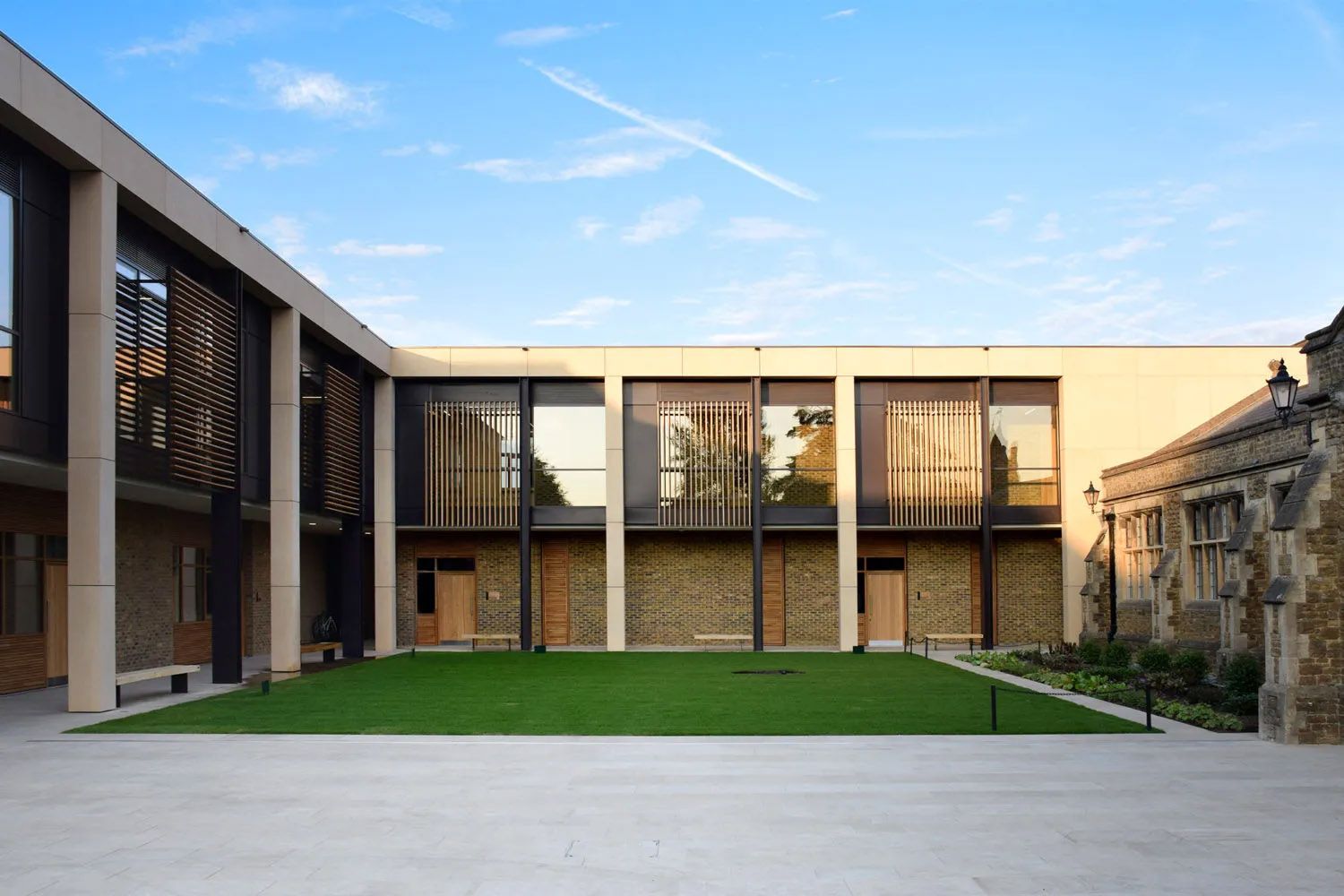 Modern courtyard building with green lawn, wooden facade details, and blue sky in an academic setting.