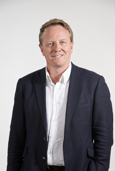 Professional businessman in navy blazer and white shirt smiling confidently against a light background.