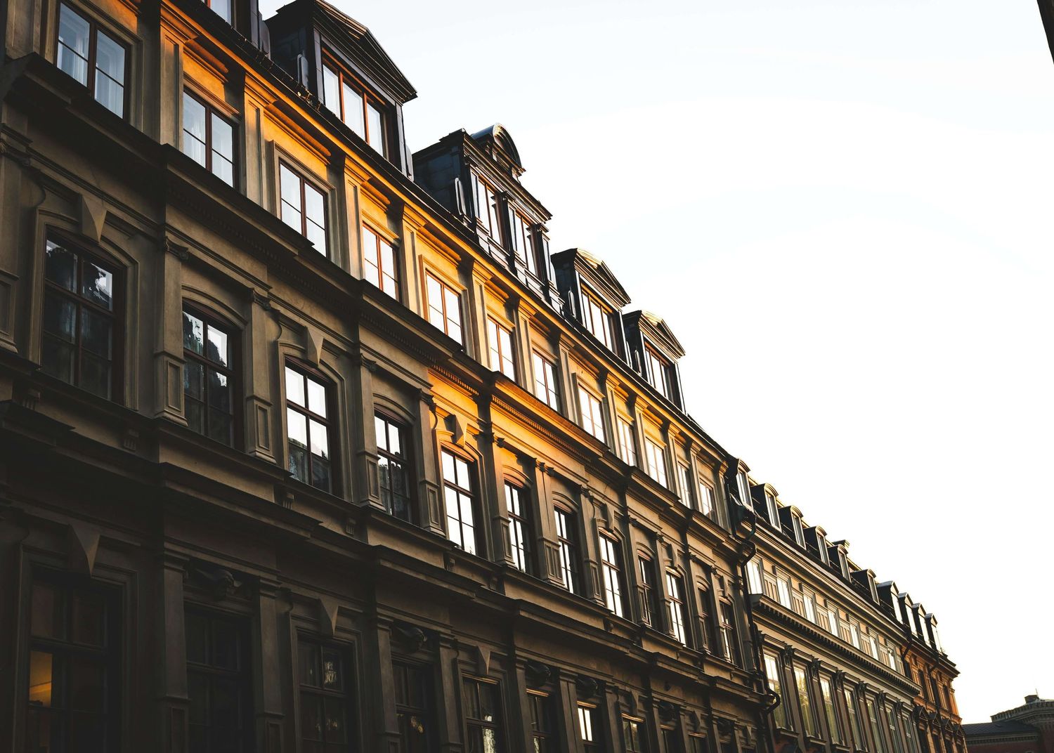 Golden sunlight illuminates the ornate facade of a classic European multi-story building with mansard roof and elegant windows.