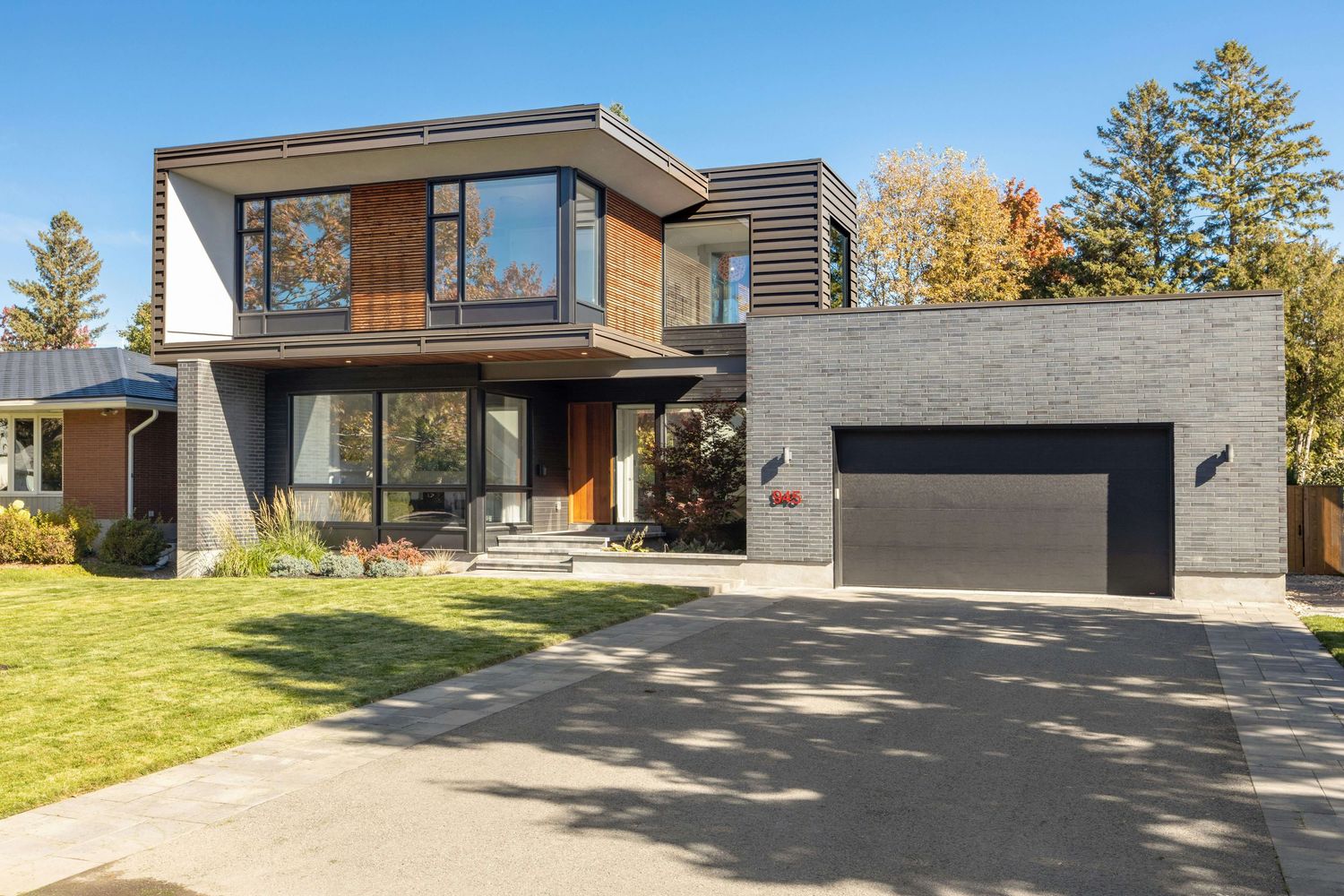 Modern two-story home with wood accents, gray stone facade, and double garage on a sunny autumn day.