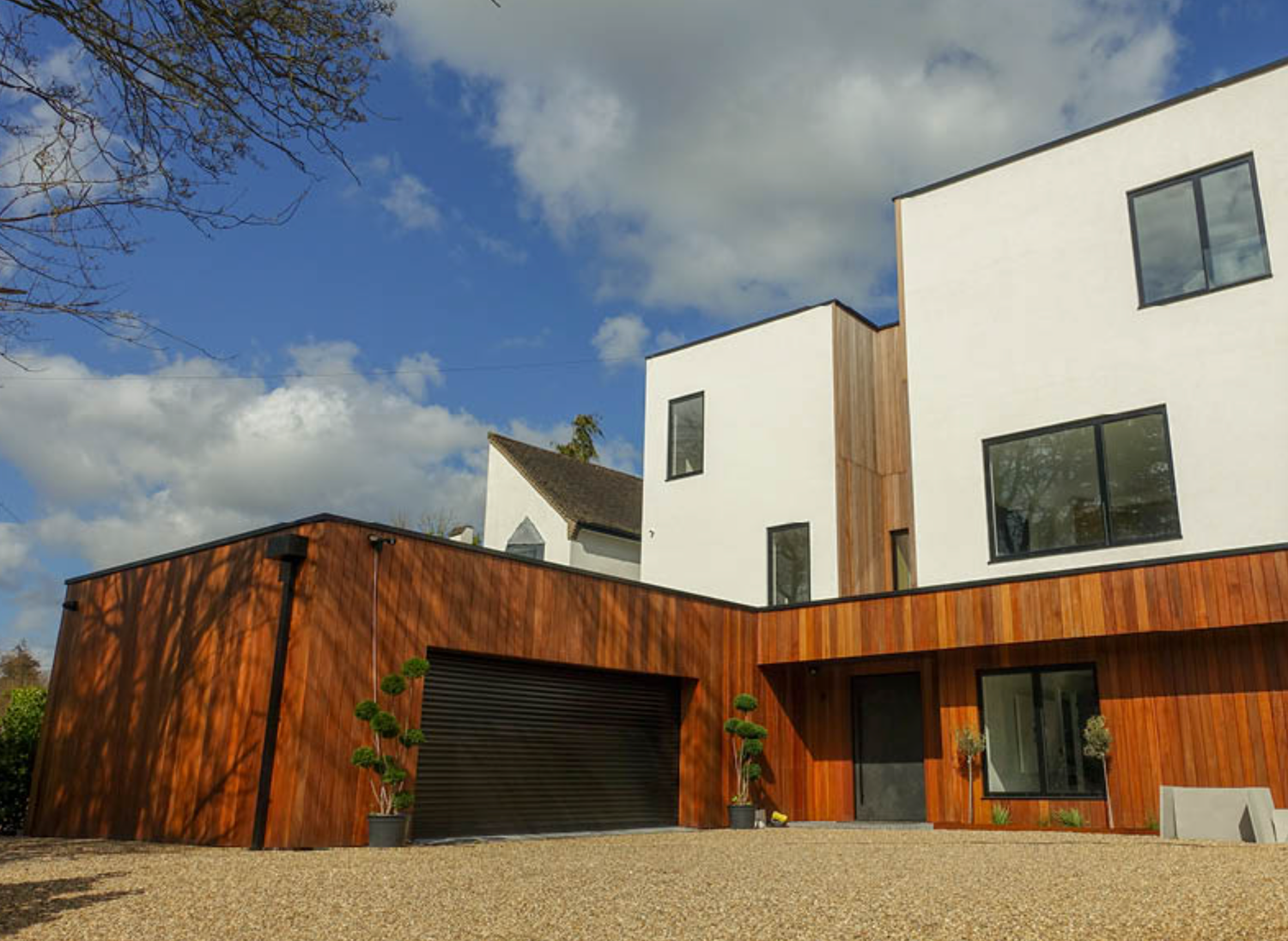 Modern two-story home with white render and warm wood cladding, featuring a double garage under blue skies.