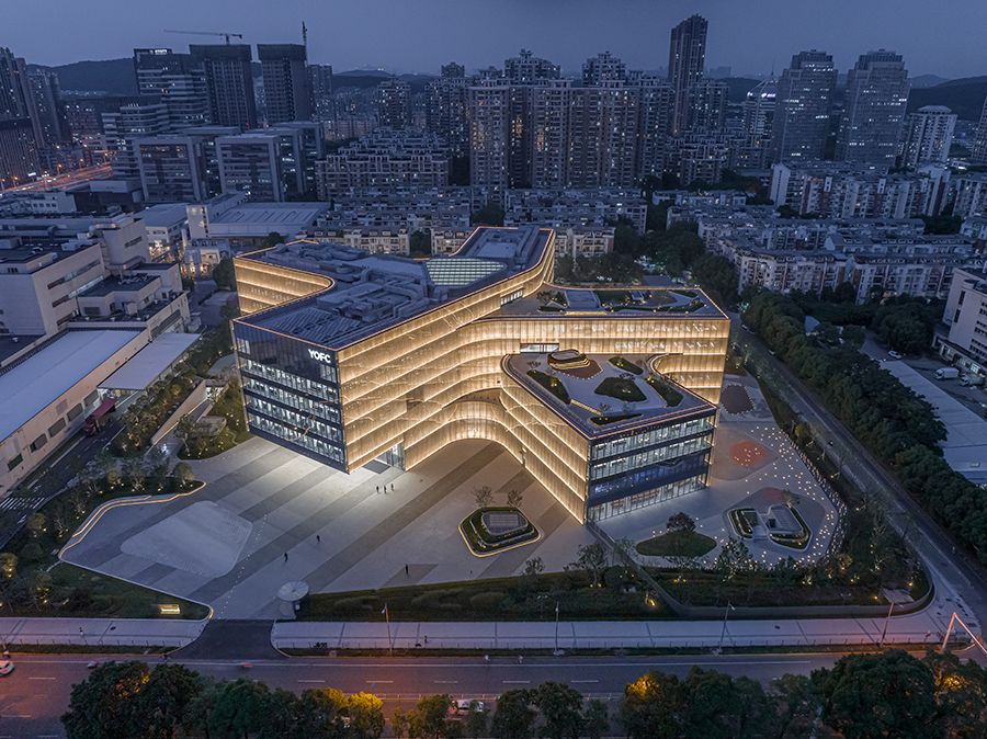 Aerial dusk view of a modern illuminated office complex with curved architecture surrounded by urban cityscape.