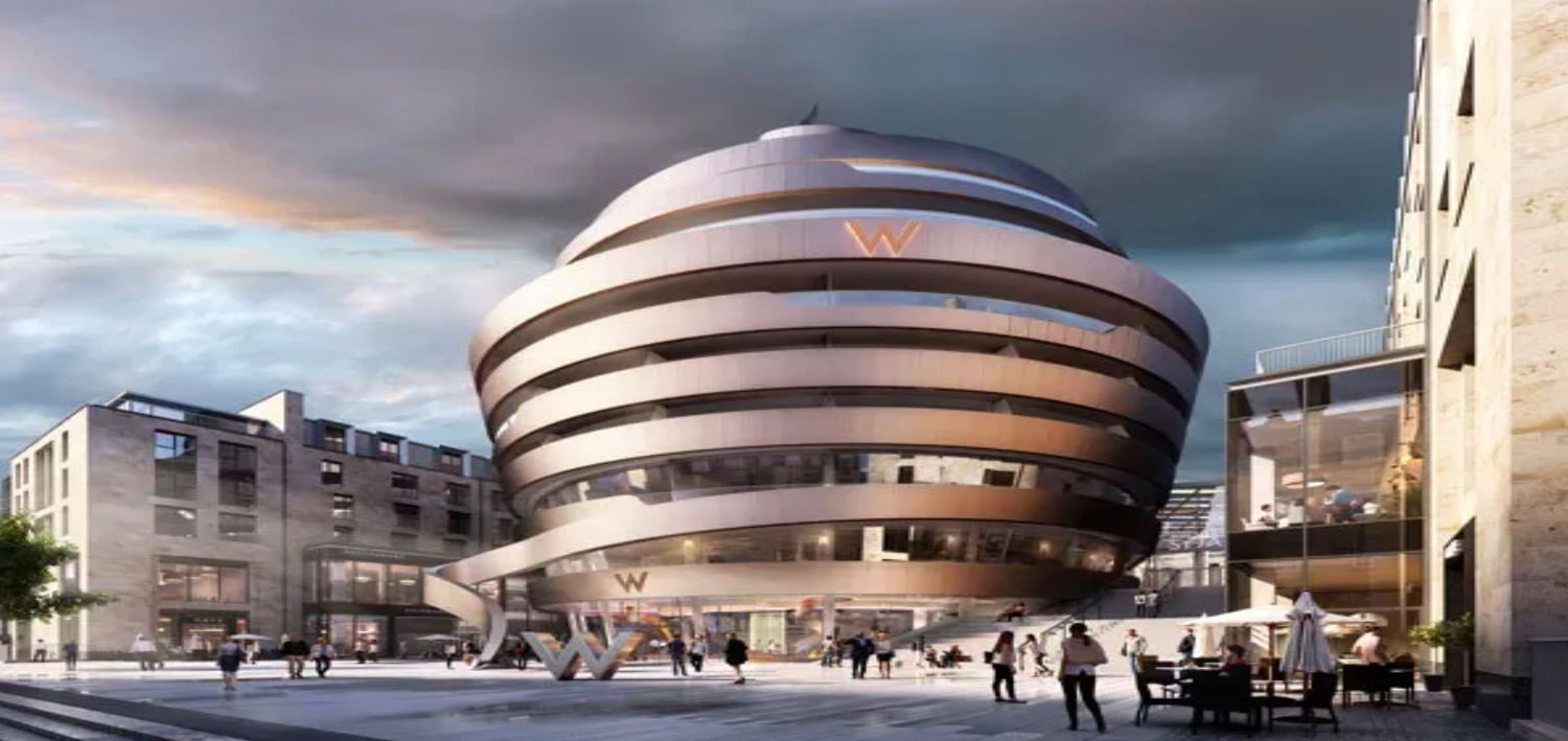 Futuristic circular building with layered facade and red logo at dusk in an urban plaza setting.