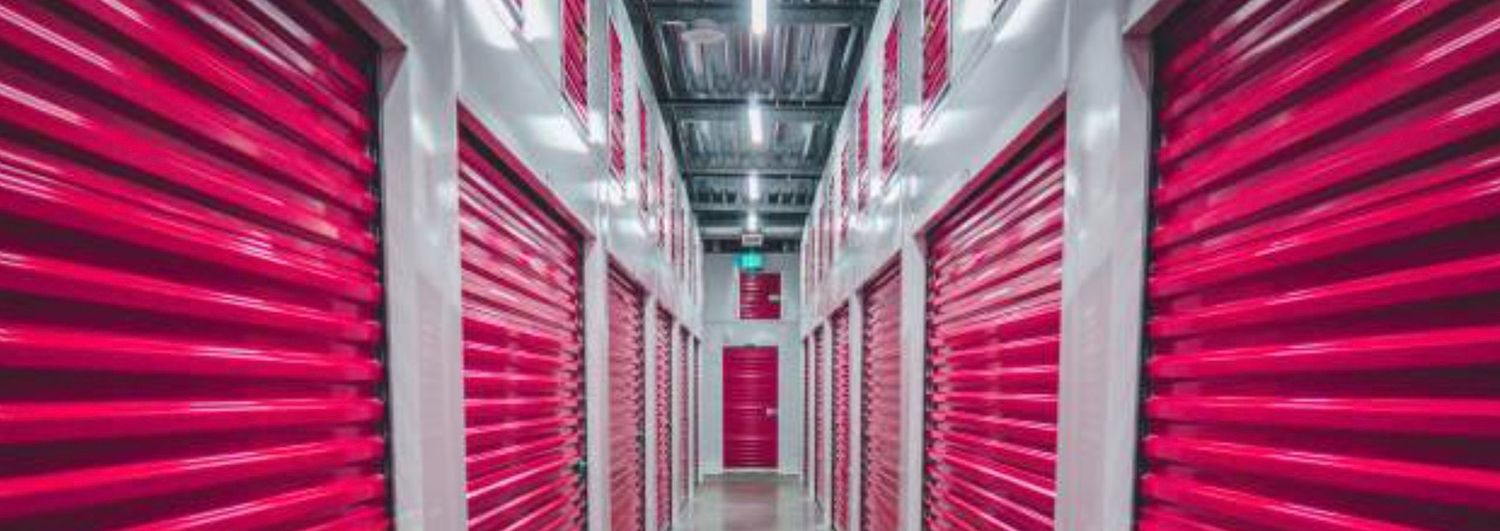 A long corridor of bright pink self-storage unit doors in a modern, well-lit indoor storage facility.