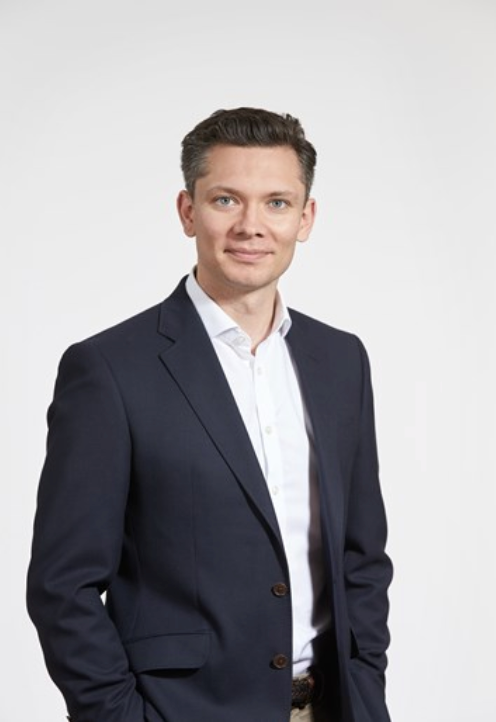 Professional businessman in navy blazer and white shirt smiling confidently against a light gray background.
