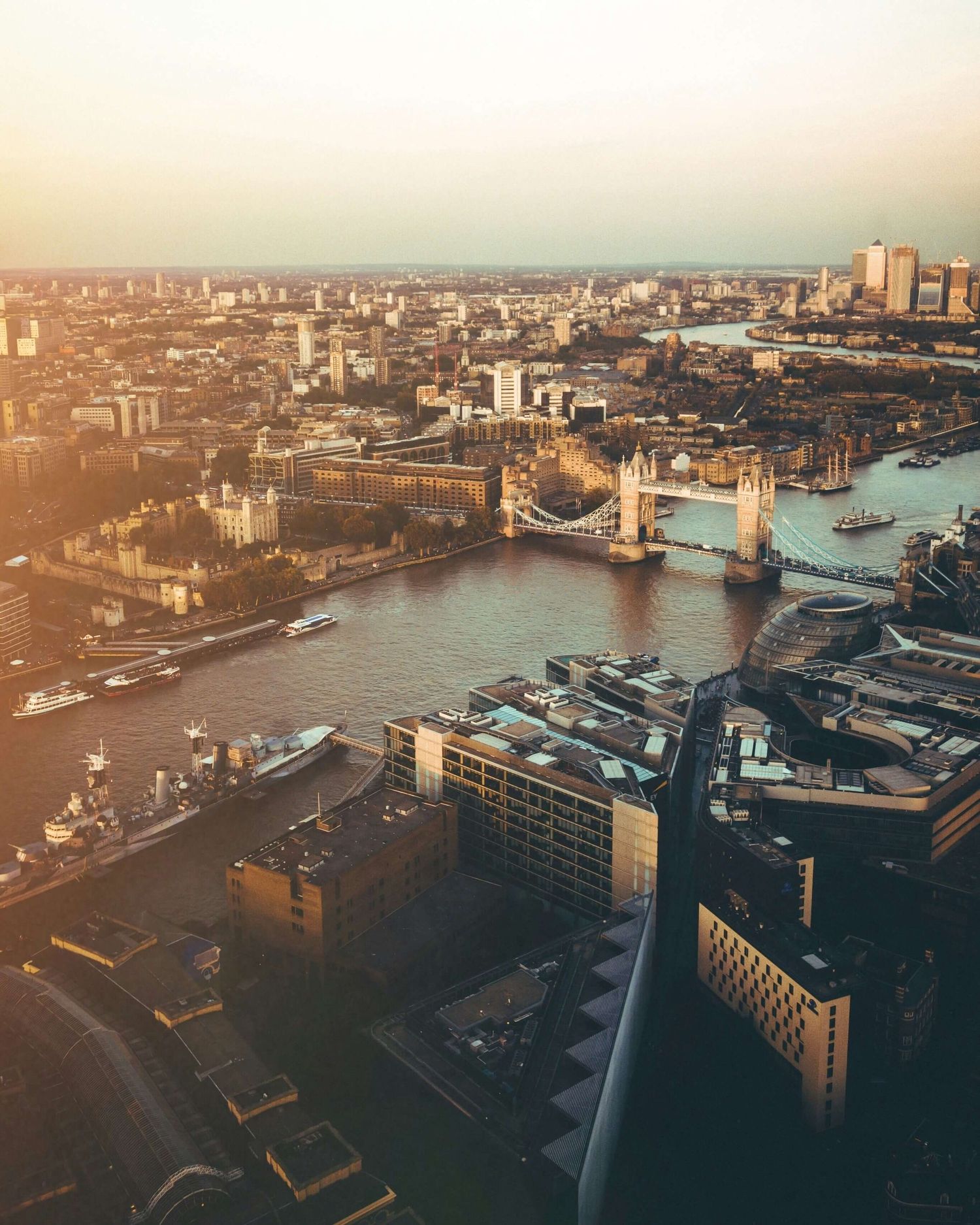 Aerial view of London skyline at sunset with Tower Bridge spanning the River Thames and city buildings stretching to horizon.
