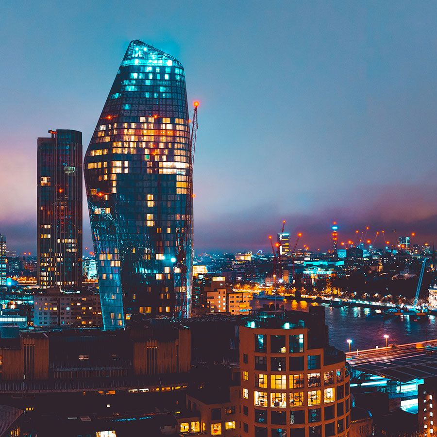 London skyline at night with illuminated skyscrapers and the iconic One Blackfriars tower glowing against a blue twilight sky.