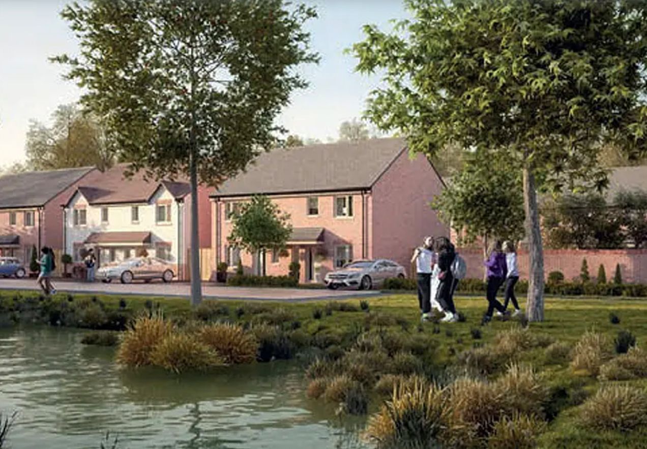 Modern residential housing development with pink brick homes, green trees, and a pond in a suburban neighborhood setting.