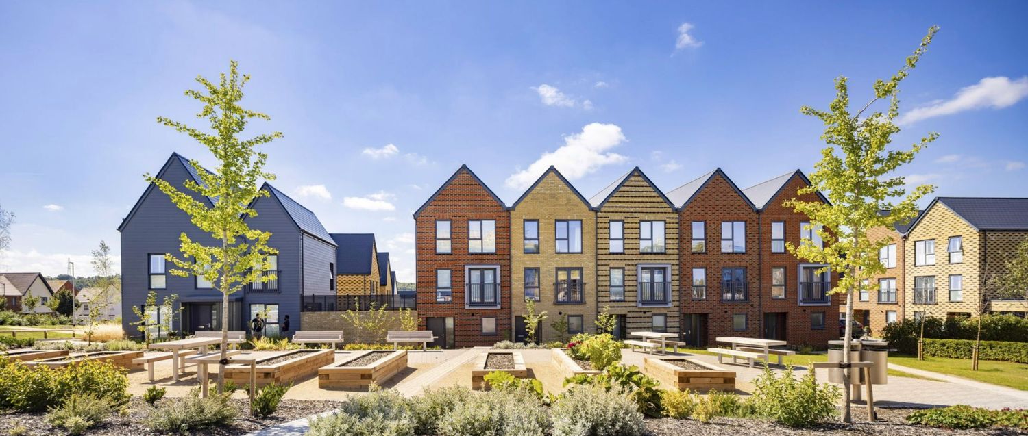 Modern brick townhouses with gabled roofs surrounding a landscaped courtyard with trees and seating areas on a sunny day.