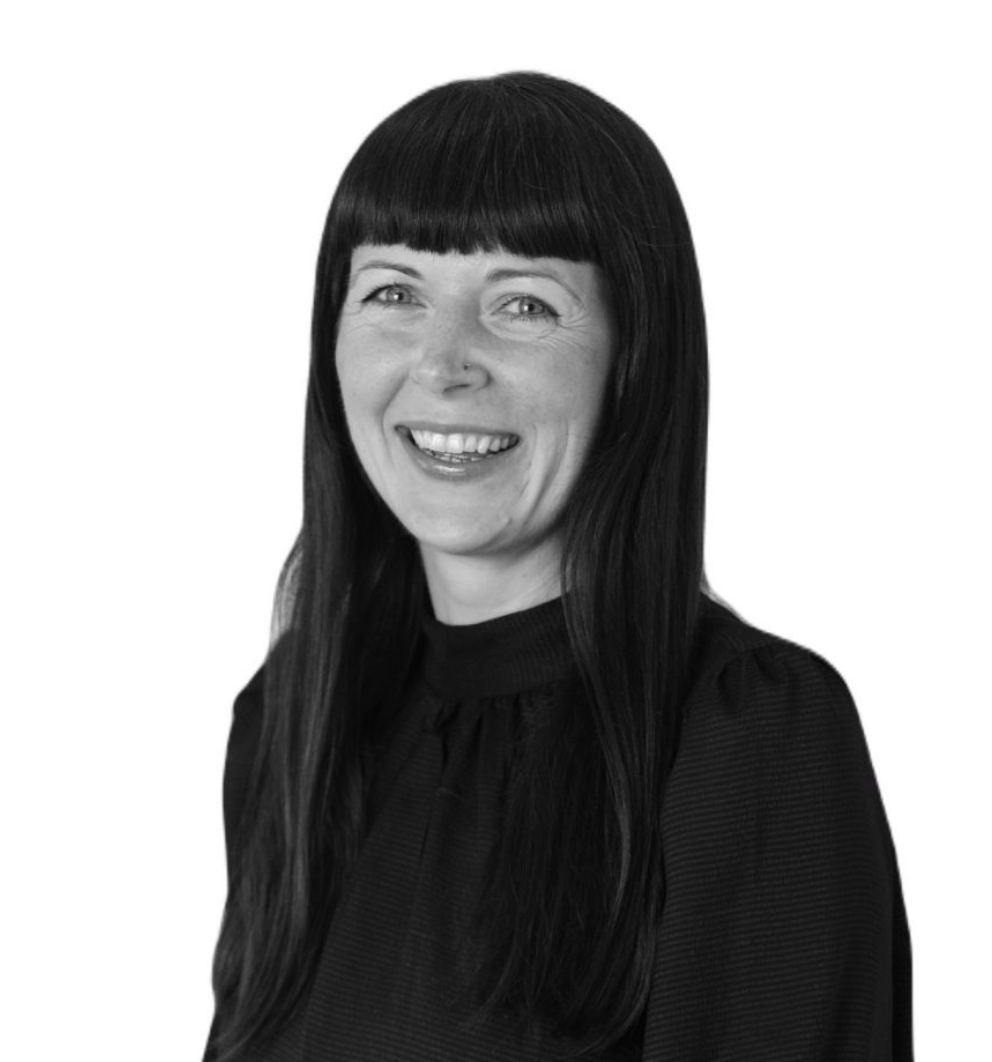 Smiling woman with dark hair and bangs wearing a black top, professional headshot in black and white.