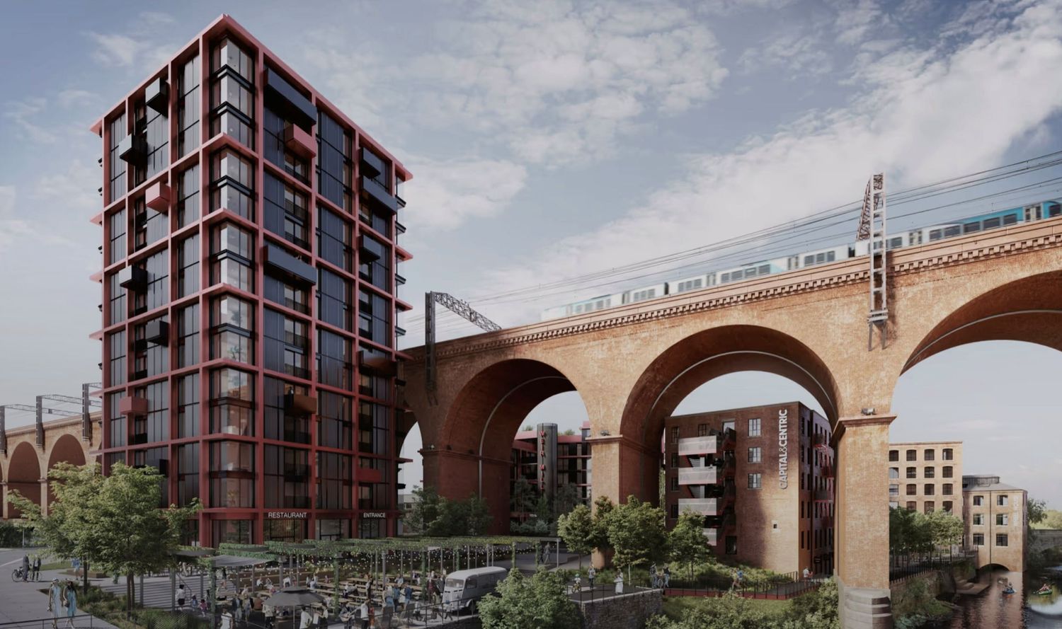 Modern red brick residential tower beside a historic railway viaduct with a passing train in an urban setting.