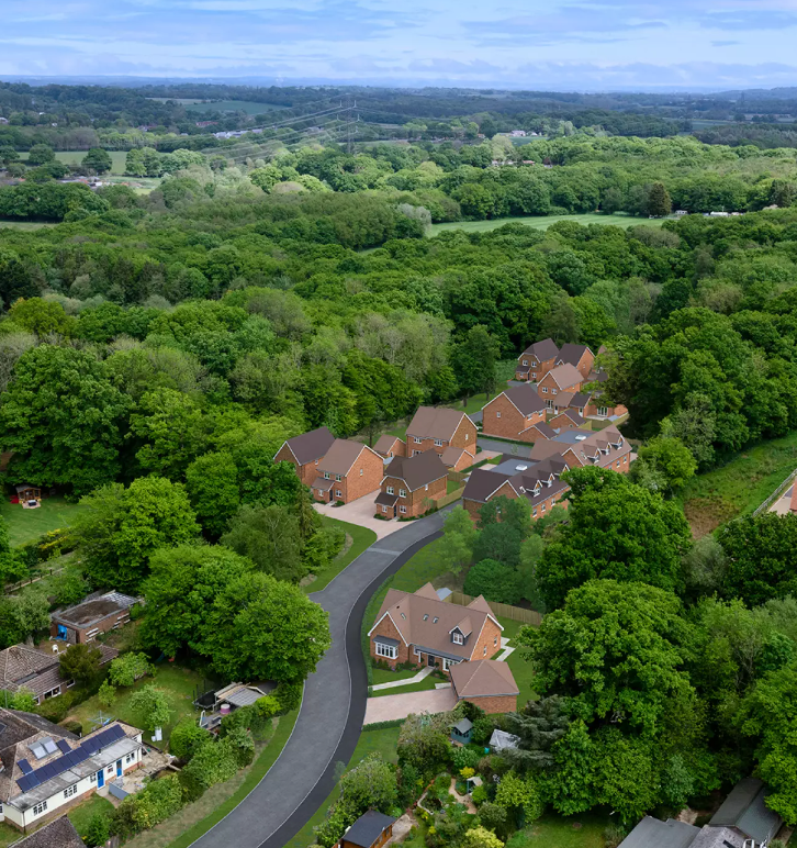 Aerial view of a residential neighborhood surrounded by lush green trees and rolling countryside in England.