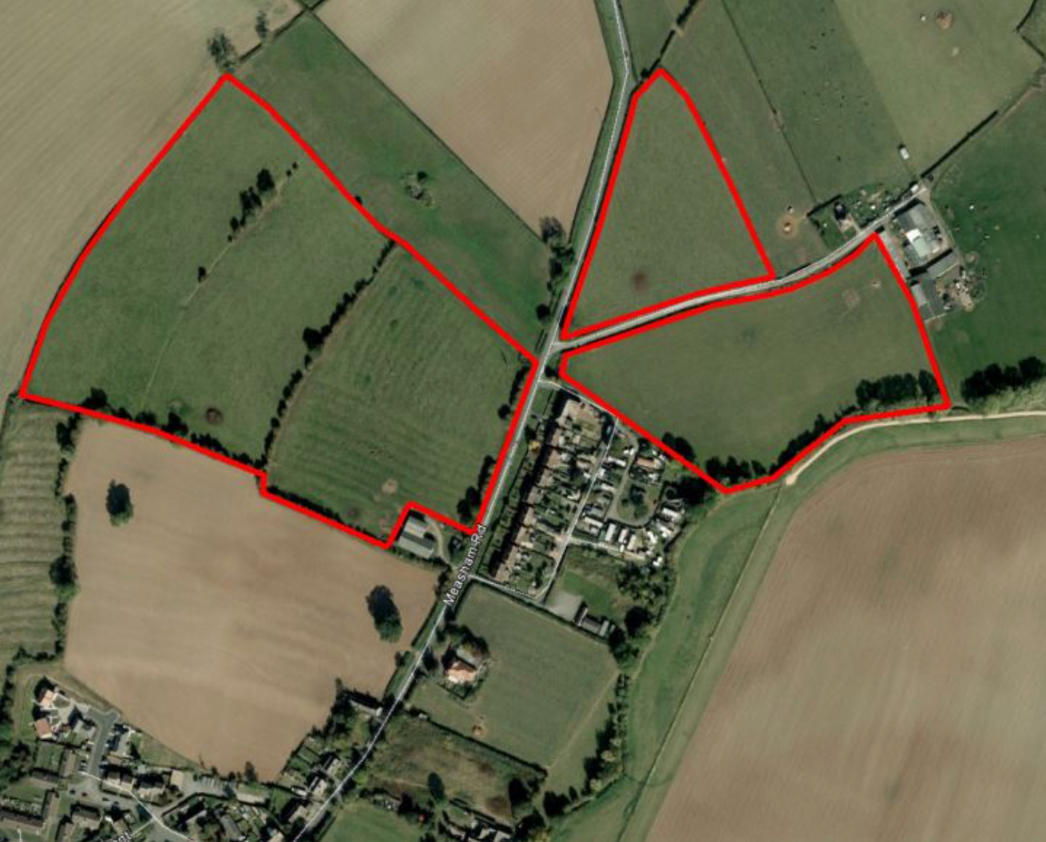 Aerial satellite view of rural farmland with red boundary lines marking property or planning zones near a small village.