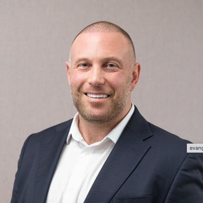 Professional headshot of a smiling bald man in a navy blazer and white shirt against a neutral background.