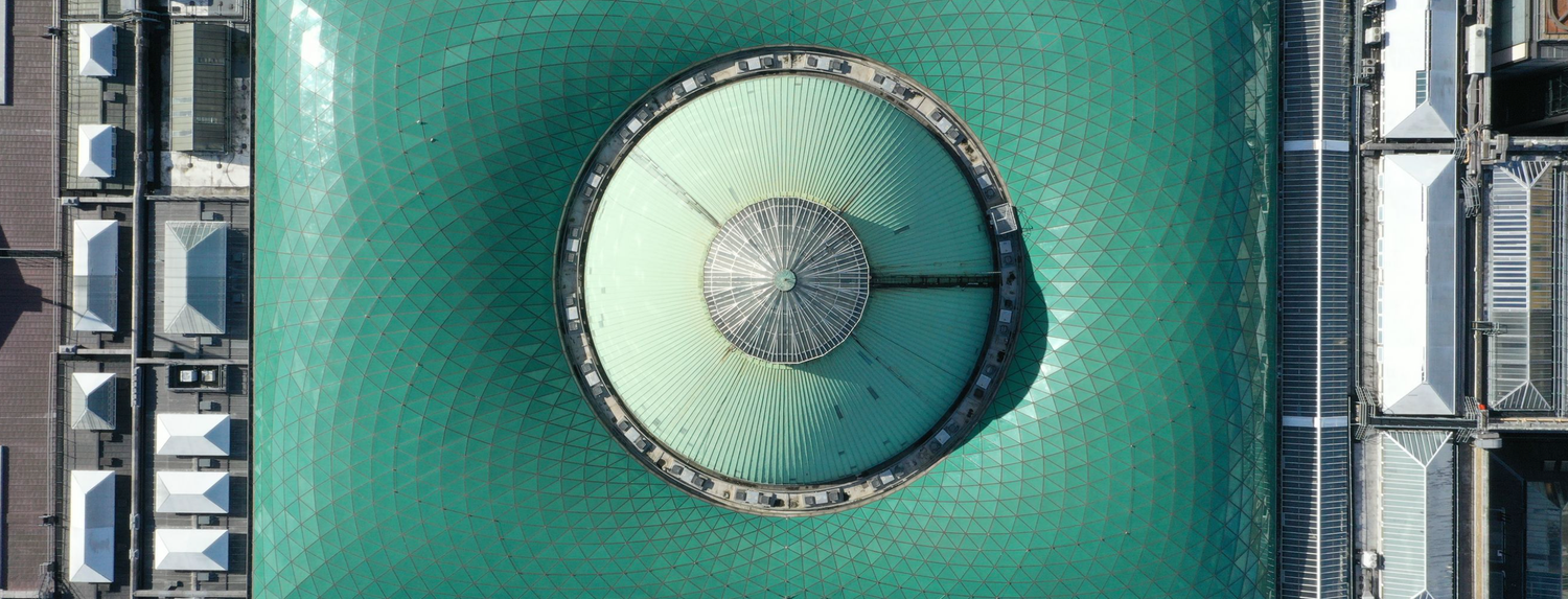 Aerial top-down view of a circular green water treatment facility surrounded by industrial buildings.