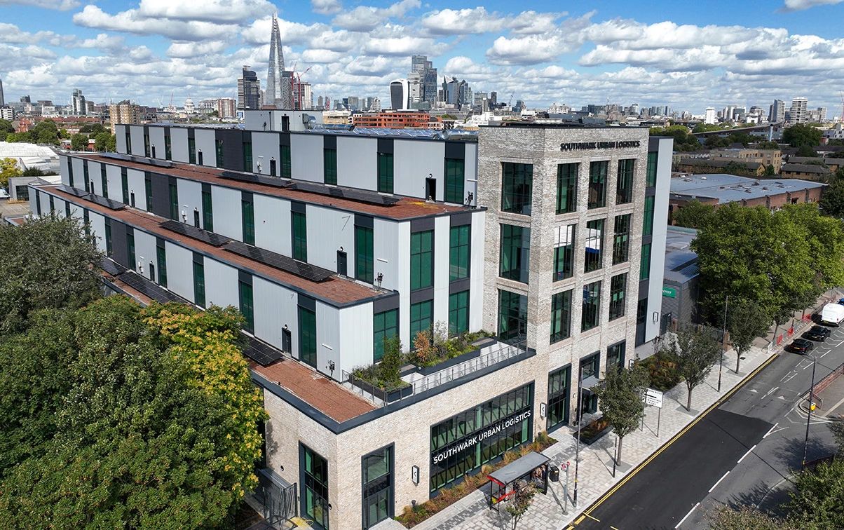 Aerial view of a modern multi-story building with green accents in Brooklyn, NYC skyline visible in background.